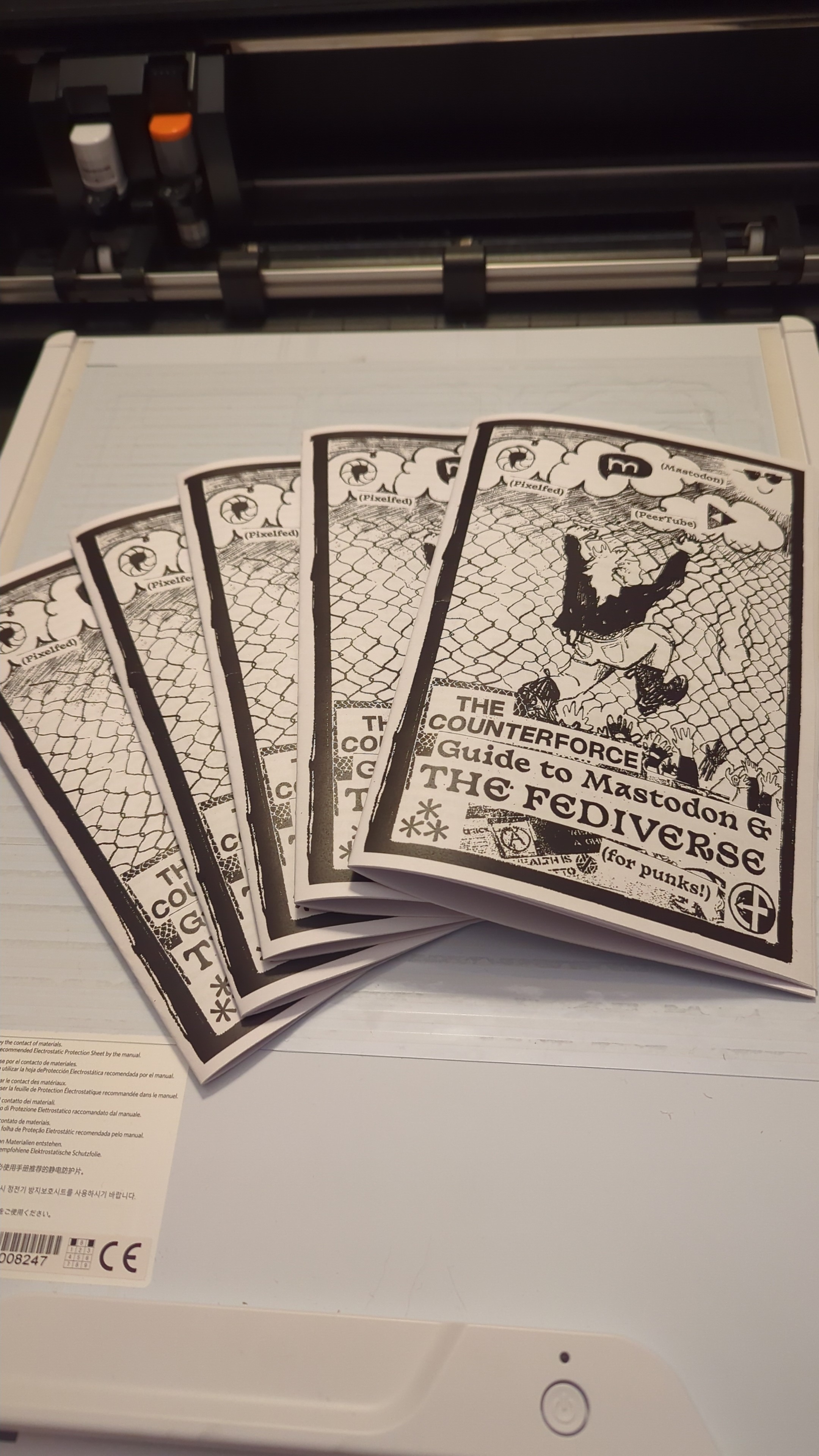 5 b&w zines splayed out in front of a Silhouette cutting machine. The zine from Counter Force is titled "Guide to Mastodon & the Fediverse".