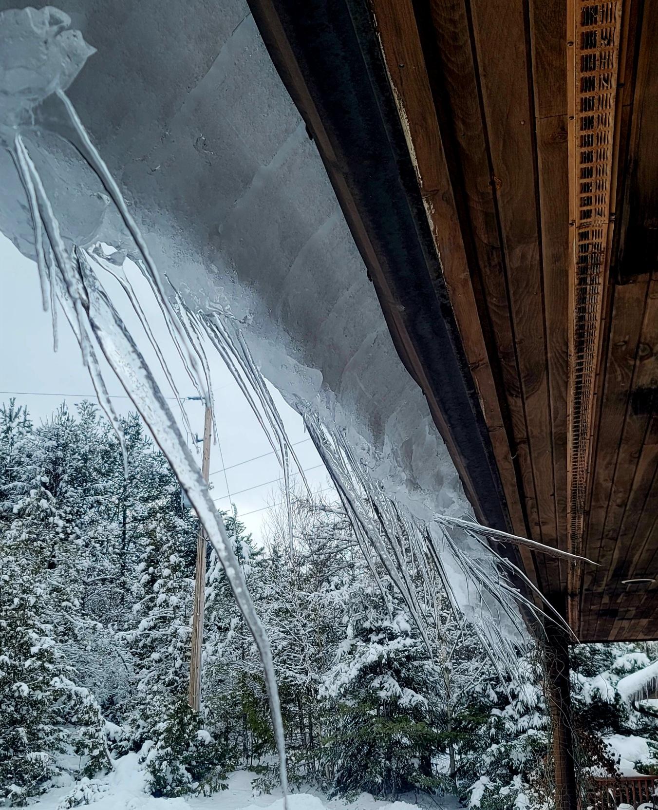Icicles hanging from a roof, some vertically, some almost horizontal as the snow curls over the edge.