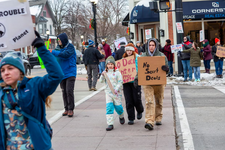 People march in street against AI data centers.