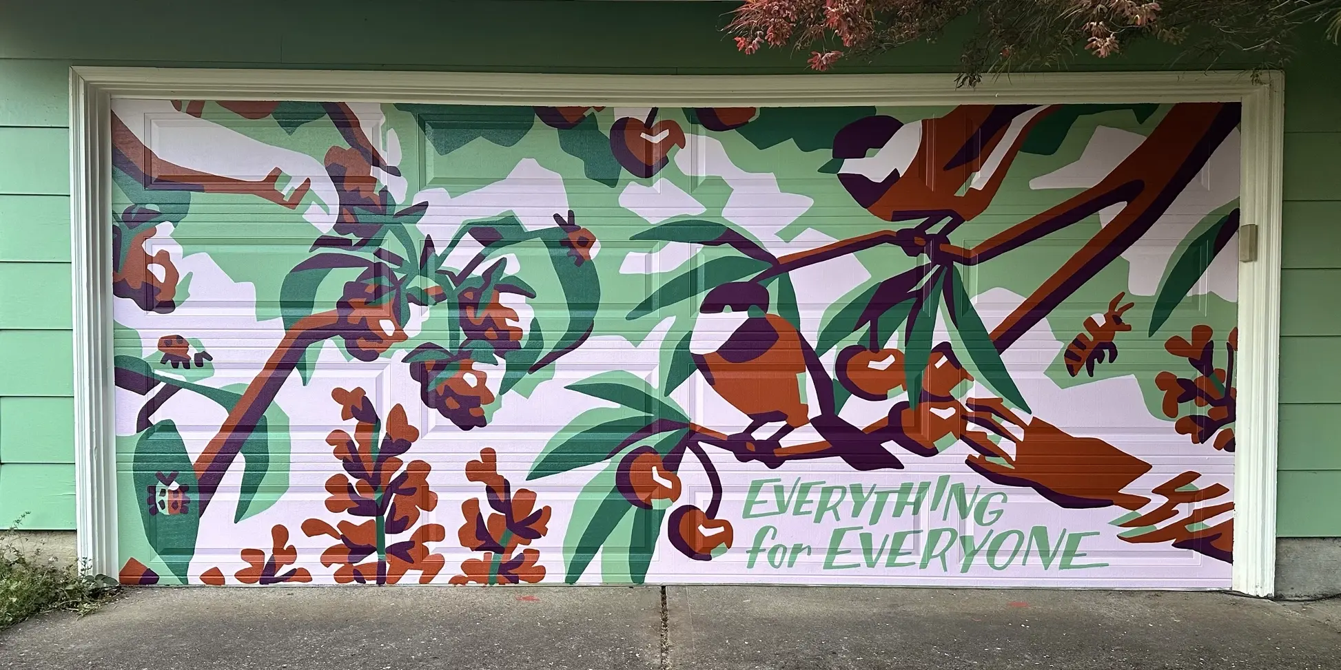 A graphic mural painted on a double garage door, featuring a human hand picking raspberries off a cane where ladybugs are crawling, beside a raccoon paw reaching for cherries hanging off a branch where two black capped chickadees are perched, as a bee hovers near sage blossoms. The mural is painted in mint green, emerald, pale pink, rust orange, and deep plum.