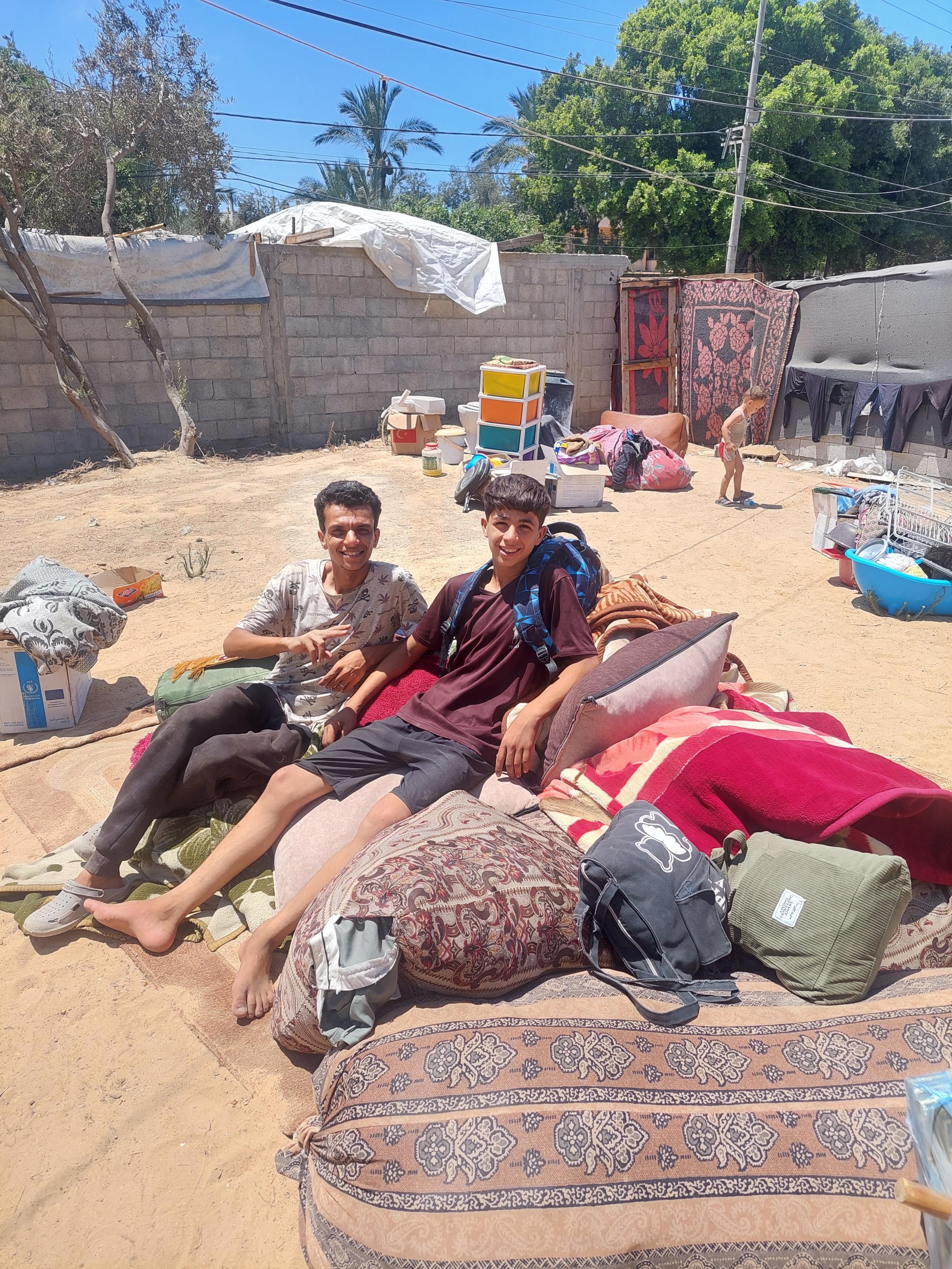 On the ground surrounded by a wall, luggage is piled up, and two young people are sitting there, smiling at the camera.