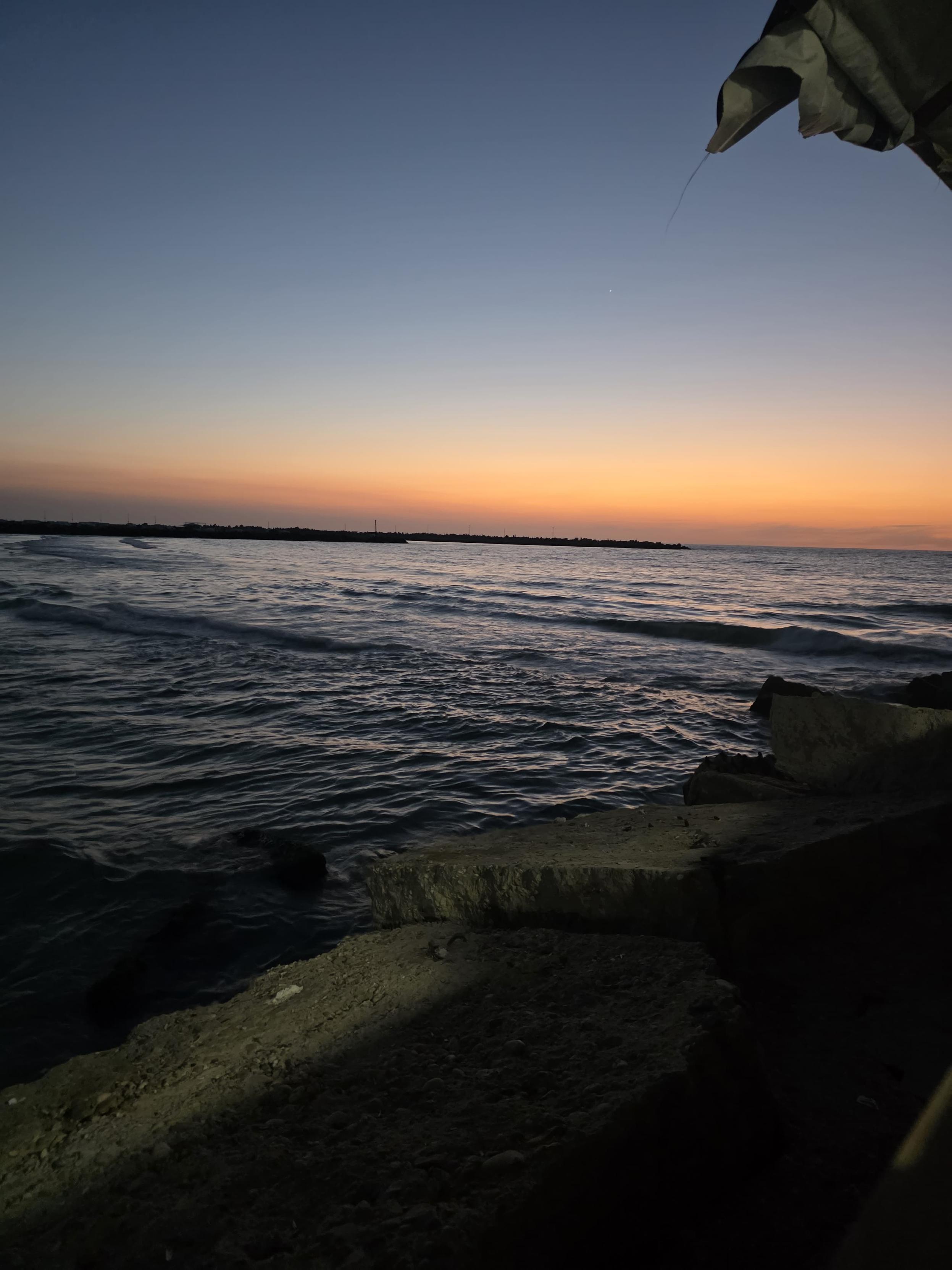 A beach at dusk.
The sky near the horizon is tinged red, while the upper part is a deep blue.