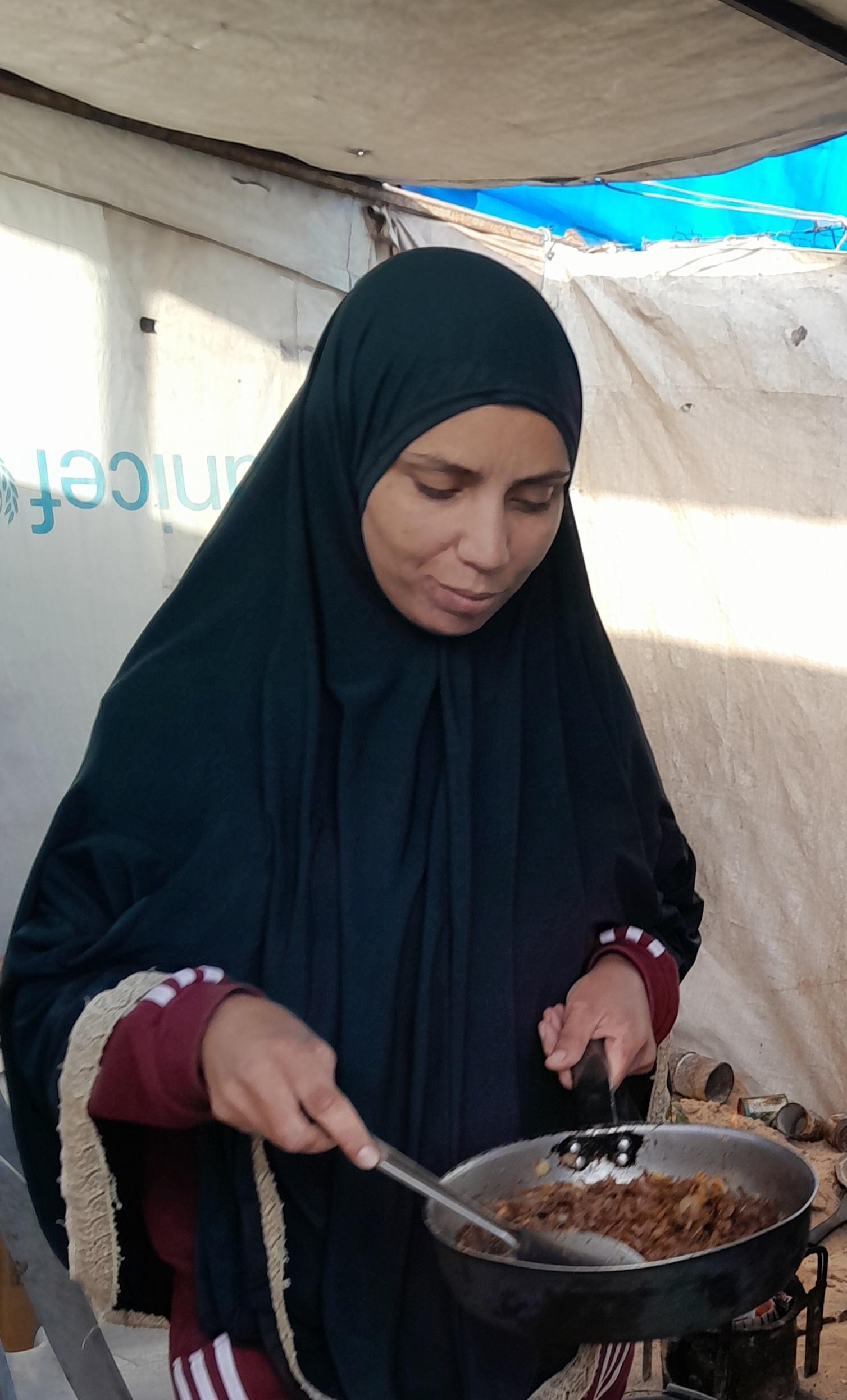 A woman wearing a black hijab is cooking in a frying pan on a stove.