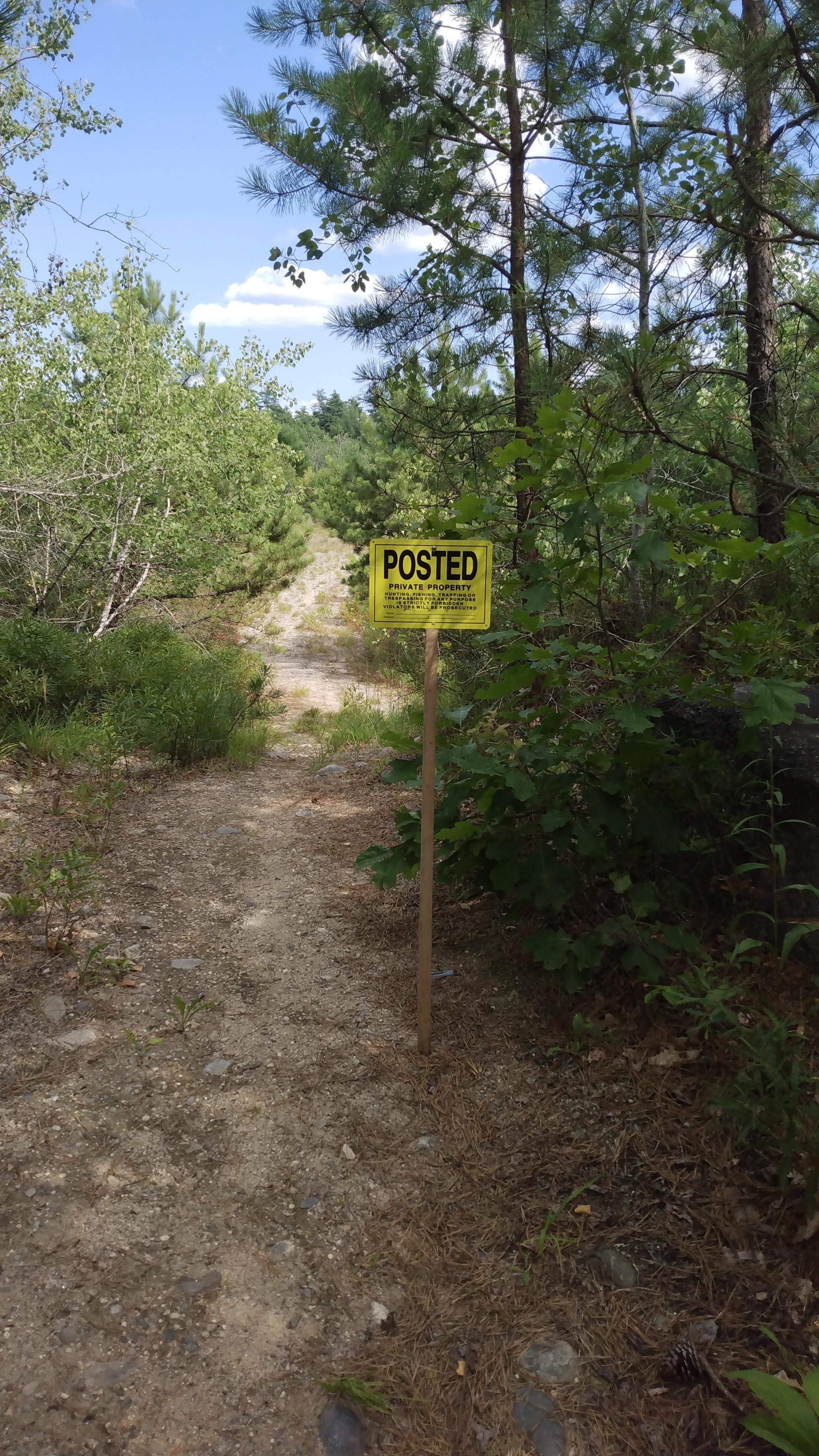 The entrance to a sand pit, which is a footpath. Next to the entrance is a "POSTED PRIVATE PROPERTY - No hunting, trespassing or fishing without permission" sign.