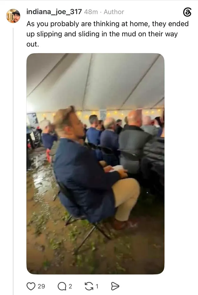 Screenshot of person at white nationalist rally in a tent on very wet and muddy ground sitting in a chair.