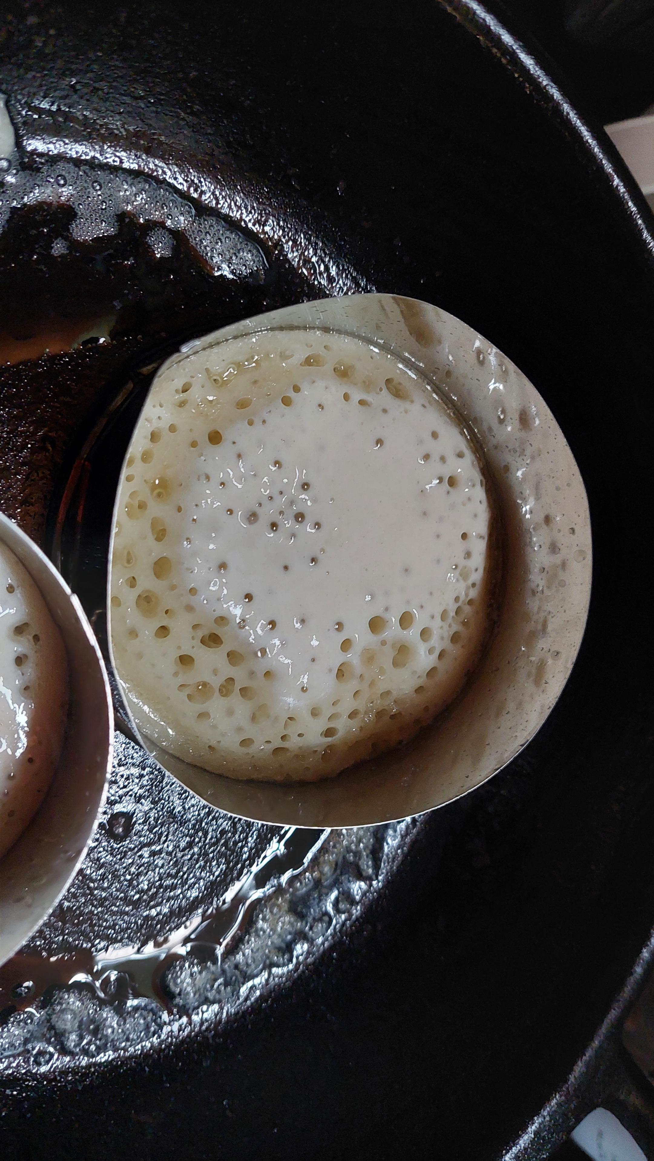 A cast iron pan with a metal ring filled with a batter that is starting to bubble