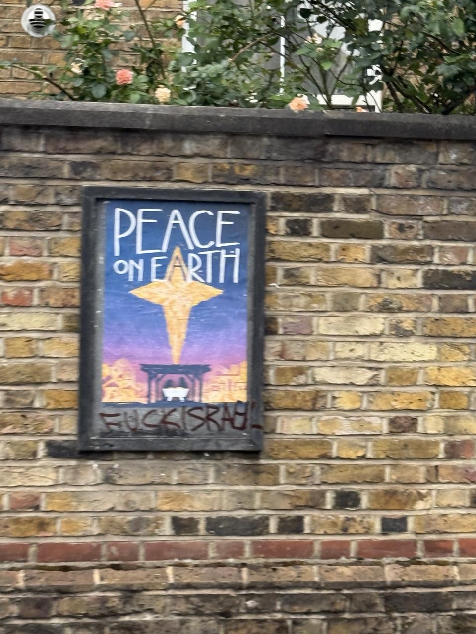 A sign on a church brick wall a star above a manger. Above - the words ‘Peace on Earth’
Below - the words “fuck israel”