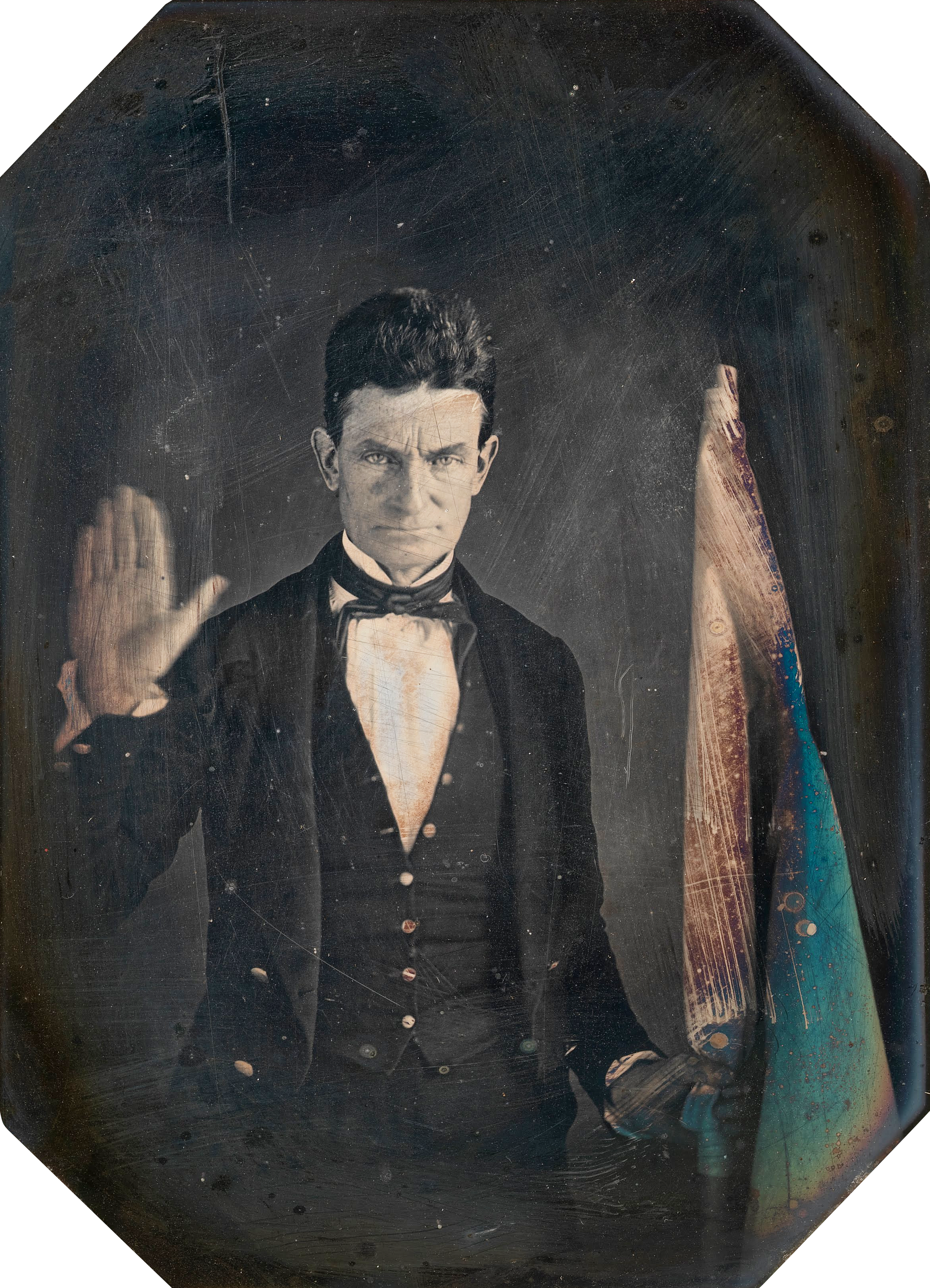A daguerreotype of Brown taken by African-American photographer Augustus Washington in Springfield, Massachusetts, c. 1846–1847. Brown is holding the hand-colored flag of Subterranean Pass Way, his militant counterpart to the Underground Railroad. By Augustus Washington - This file has been extracted from another file, Public Domain, https://commons.wikimedia.org/w/index.php?curid=12020940